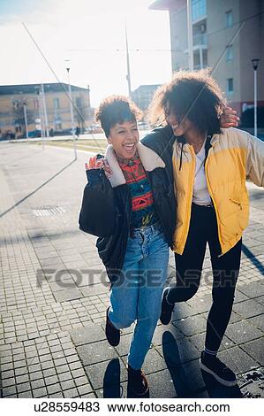 Stock Image - Two cool young female friends laughing on urban sidewalk. Fotosearch