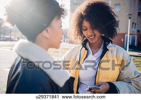 Two cool young female friends looking at smartphone in urban street View Large Photo Image Stock Image - Two cool young female friends looking at smartphone in urban street. Fotosearch