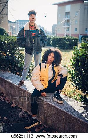 Stock Image - Two cool young female friends on urban wall, portrait. Fotosearch