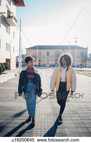 Stock Photography - Two cool young female friends strolling on urban sidewalk, full length. Fotosearch