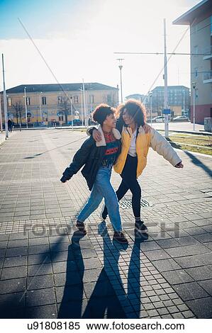 Stock Photography - Two cool young female friends strolling and laughing on urban sidewalk. Fotosearch