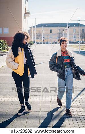 Two cool young female friends walking and talking on urban sidewalk View Large Photo Image Stock Image - Two cool young female friends walking and talking on urban sidewalk. Fotosearch