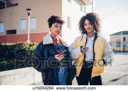 Picture - Two cool young female friends with smartphones on urban sidewalk, portrait. Fotosearch