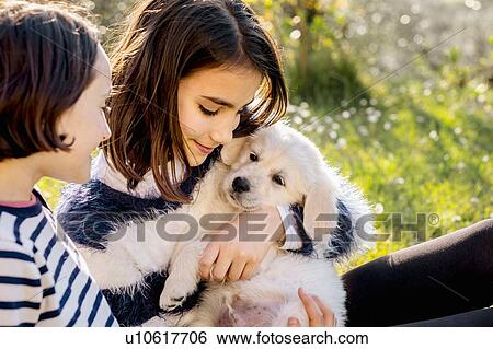Two girls sitting in orchard hugging a cute golden retriever puppy, Scandicci, Tuscany, Italy View Large Photo Image Stock Photograph - Two girls sitting in orchard hugging a cute golden retriever puppy, Scandicci, Tuscany, Italy. Fotosearch