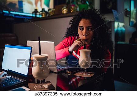 Stock Photography - Two women at cafe table drinking smoothie and typing on laptop. Fotosearch
