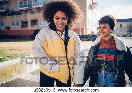 Two young female friends strolling on urban sidewalk View Large Photo Image Stock Image - Two young female friends strolling on urban sidewalk. Fotosearch
