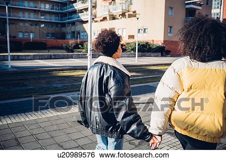 Two young female friends strolling on urban sidewalk, rear view View Large Photo Image Stock Photograph - Two young female friends strolling on urban sidewalk, rear view. Fotosearch