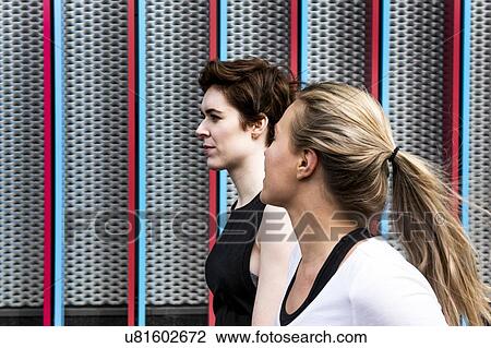 Stock Image - Two young female runners talking on city sidewalk, head and shoulders. Fotosearch