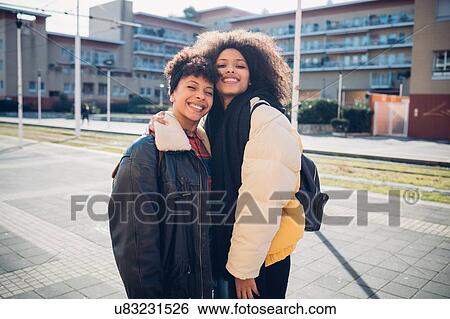 Stock Photograph - Two young women posing on urban sidewalk, portrait. Fotosearch