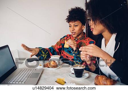 Two young women talking at looking at laptop in cafe View Large Photo Image Picture - Two young women talking at looking at laptop in cafe. Fotosearch