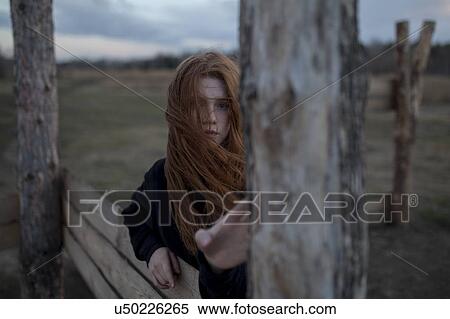 Stock Photography - Windswept teenage girl by tree trunk. Fotosearch