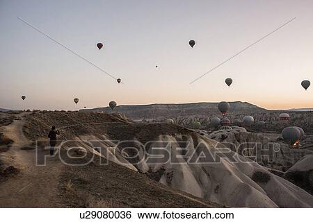 Stock Photograph - Woman enjoying view and display of hot air balloons in valley, Greme, Cappadocia, Nevsehir, Turkey. Fotosearch