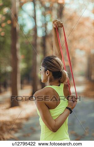 Stock Image - Woman exercising with resistance band outdoors. Fotosearch