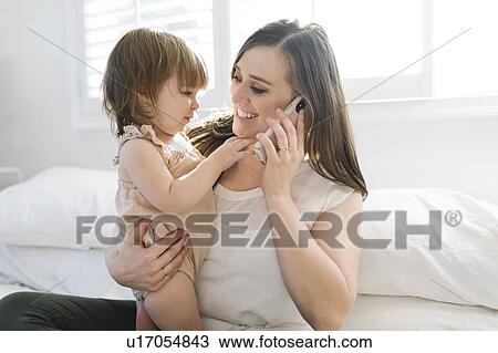 Stock Image - Woman holding daughter while on phone call. Fotosearch