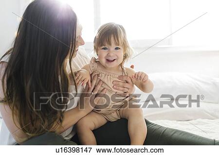 Woman holding her daughter on bed View Large Photo Image Stock Photo - Woman holding her daughter on bed. Fotosearch