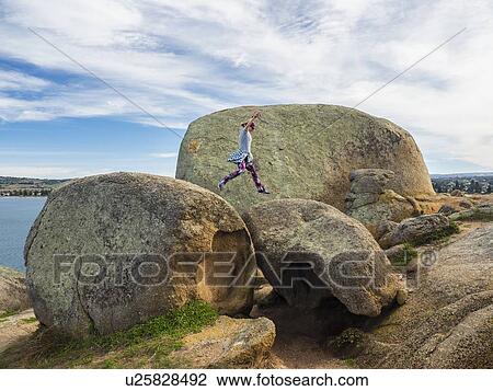 Stock Image - Woman jumping on boulders on Granite Island, Australia. Fotosearch