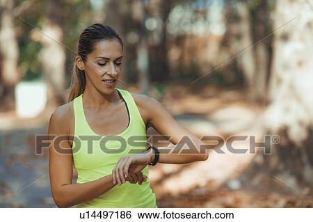 Stock Photograph - Woman looking at smart watch after outdoor training. Fotosearch