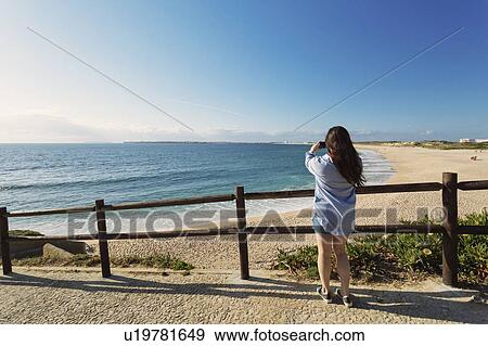 Stock Photo - Woman photographing beach in Lisbon, Portugal. Fotosearch
