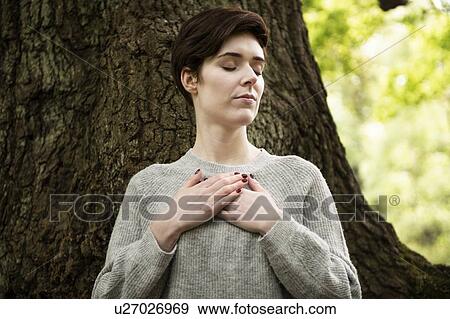 Stock Photo - Woman practising Reiki, large tree trunk in background. Fotosearch