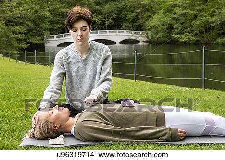 Woman practising Reiki on grass lawn by river, London, UK View Large Photo Image Picture - Woman practising Reiki on grass lawn by river, London, UK. Fotosearch