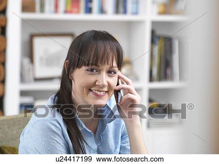 Stock Photo - Woman relaxing and catching up with friends over the phone in her lounge. Fotosearch