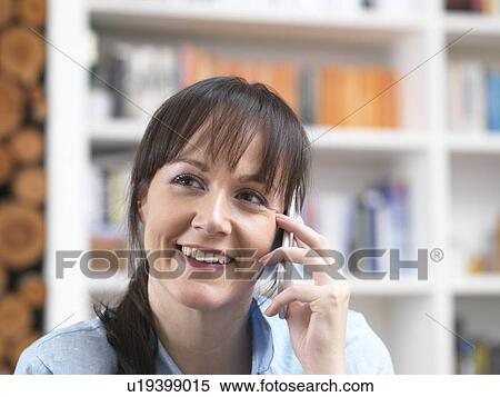 Stock Photography - Woman relaxing and catching up with friends over the phone in her lounge. Fotosearch