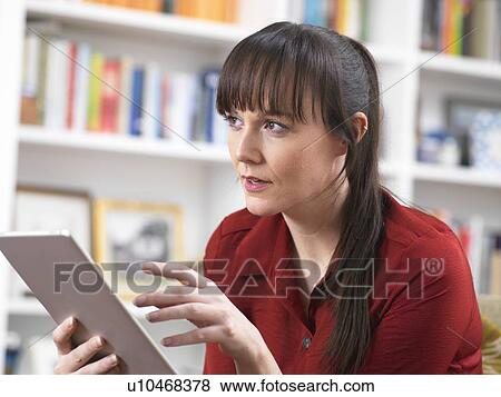 Stock Photo - Woman relaxing at home on her digital tablet which she uses for social media, email and internet shopping. Fotosearch