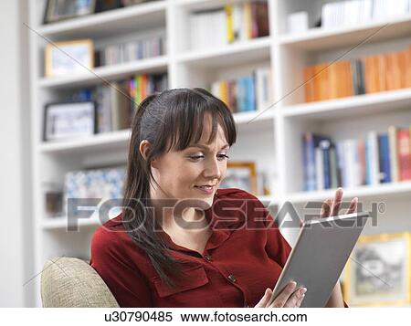 Woman relaxing at home on her digital tablet which she uses for social media, email and internet shopping View Large Photo Image Stock Photography - Woman relaxing at home on her digital tablet which she uses for social media, email and internet shopping. Fotosearch