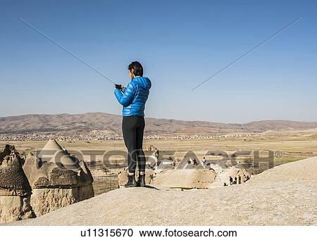 Stock Image - Woman taking photograph of fairy chimney, Greme, Cappadocia, Nevsehir, Turkey. Fotosearch