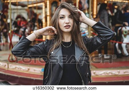 Stock Image - Woman touching hair and posing in front of carousel. Fotosearch