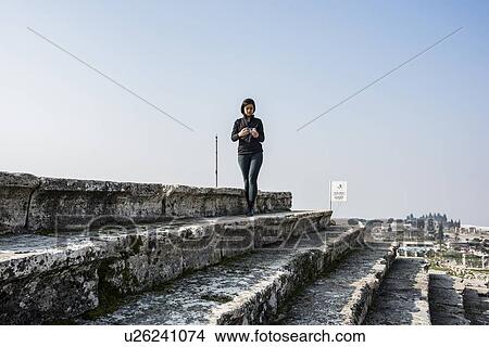 Picture - Woman using smartphone on steps, Pamukkale, Denizli, Turkey. Fotosearch
