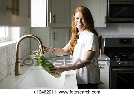 Stock Image - Woman washing celery in kitchen sink. Fotosearch