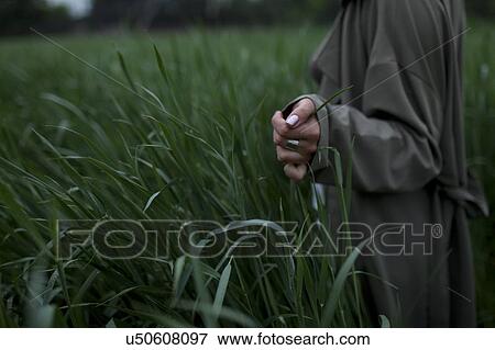 Stock Photo - Woman wearing green coat walking through field. Fotosearch