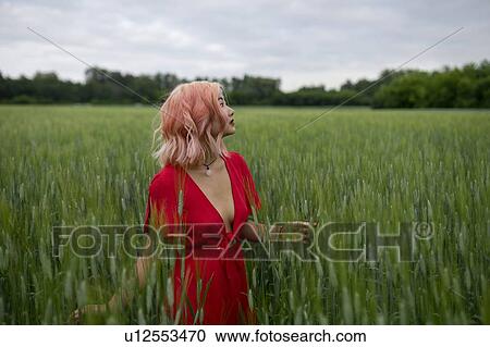 Stock Image - Woman with pink hair wearing red dress in wheat field. Fotosearch