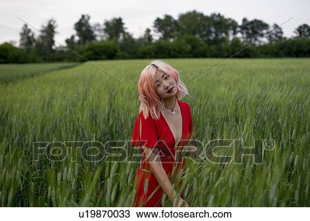 Stock Image - Woman with pink hair wearing red dress in wheat field. Fotosearch