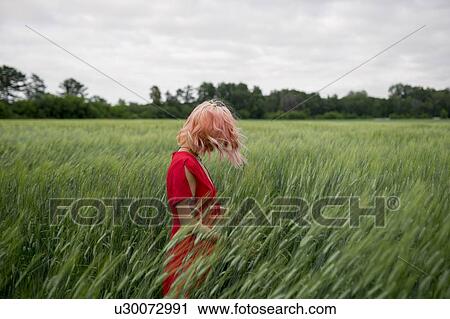 Stock Image - Woman with pink hair wearing red dress in wheat field. Fotosearch