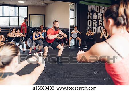 Stock Photo - Women doing squat training in gym with male trainer. Fotosearch