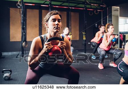 Stock Photo - Women training in gym, squatting and lifting kettle bells. Fotosearch