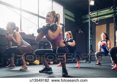Stock Image - Women training in gym, squatting with kettle bells. Fotosearch