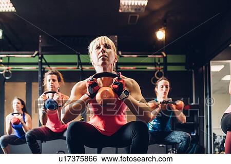 Stock Photograph - Women training in gym, squatting with kettle bells. Fotosearch