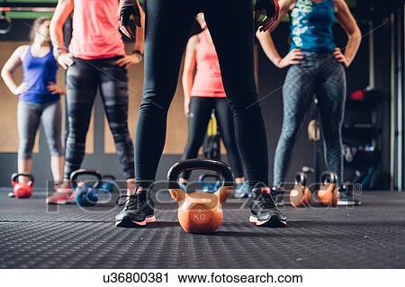 Stock Image - Women training in gym, standing by kettle bells, surface level. Fotosearch