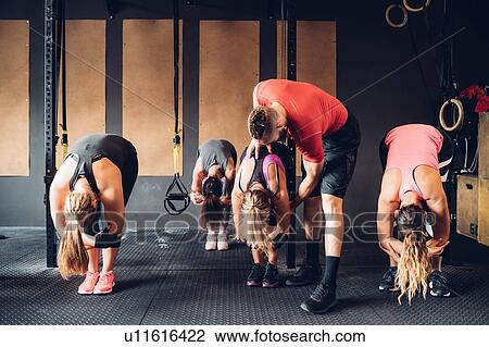 Stock Image - Women training in gym with male trainer, bending forward. Fotosearch