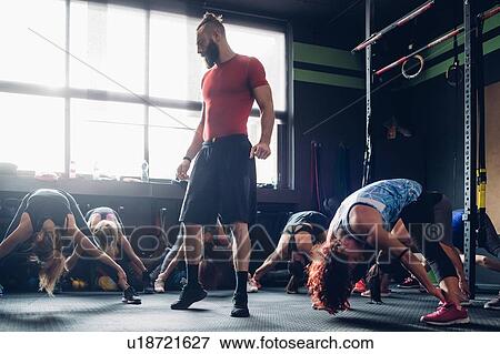 Stock Photo - Women training in gym with male trainer, bending forward with legs outstretched. Fotosearch