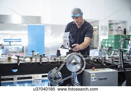 Stock Photography - Worker adjusting printing machine in print factory. Fotosearch