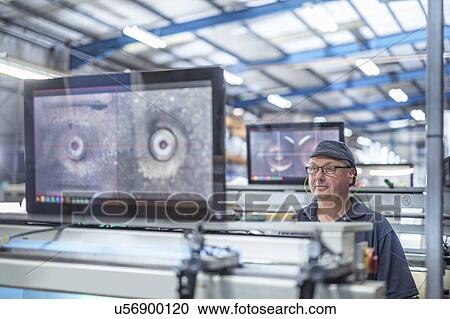 Stock Image - Worker aligning print surface on rollers in print factory. Fotosearch