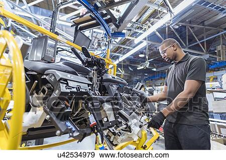 Stock Photo - Worker assembling dashboard on production line in car factory. Fotosearch