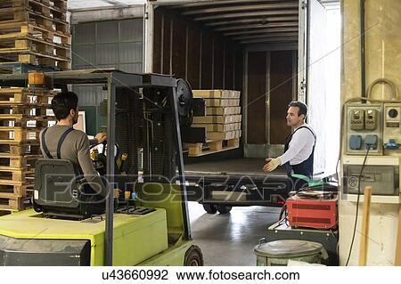 Worker guiding forklift driver towards truck in factory View Large Photo Image Stock Image - Worker guiding forklift driver towards truck in factory. Fotosearch