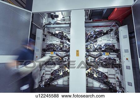 Stock Photo - Worker inserting print rollers into printing machine in print factory, motion blur. Fotosearch
