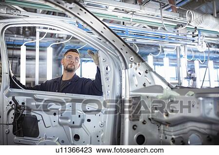 Stock Image - Worker inspecting car body in car factory. Fotosearch