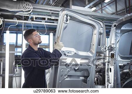 Stock Image - Worker inspecting car body in car factory. Fotosearch